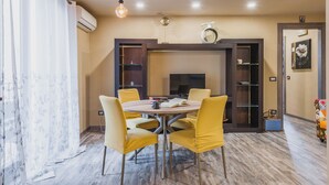 A dining area with a round table, four yellow chairs, a fireplace, and a bookshelf. - Ursino apartment with balcony by Wonderful Italy (Catania)