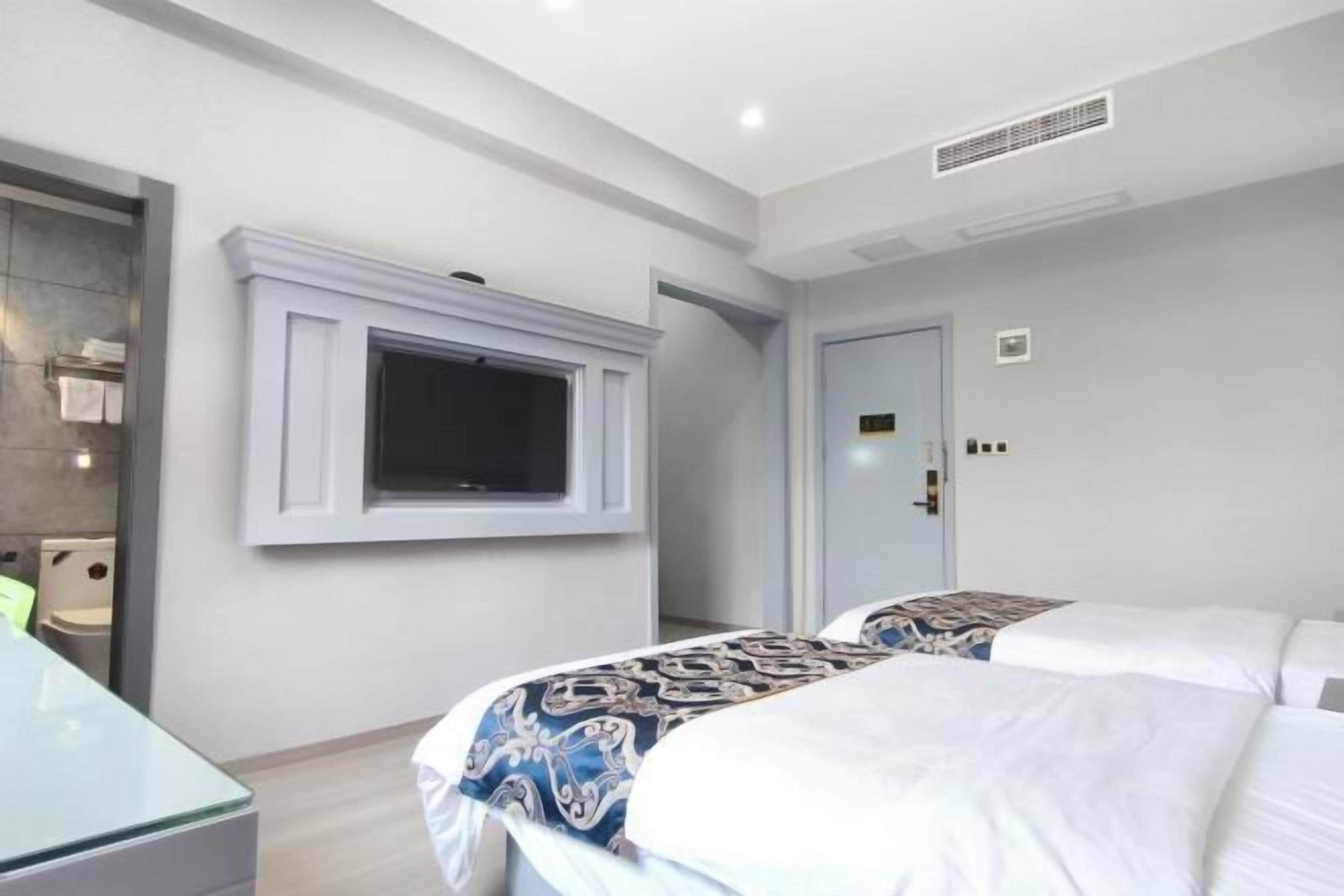 Una camera d'albergo con due letti, una TV montata a parete, una porta con serratura e un piccolo tavolo.