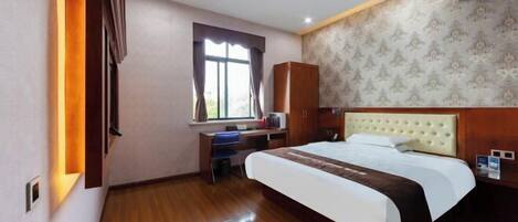A hotel room with a large bed, a desk, a wardrobe, and a window with curtains.