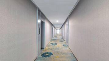 A long, narrow hotel corridor with doors on both sides and a carpeted floor.