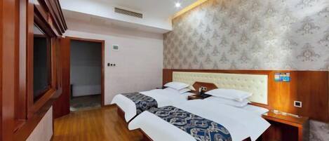A hotel room with two beds, wooden flooring, a patterned wallpaper on the wall, and a small bedside table with a phone.
