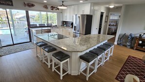 A modern kitchen with a large island, white cabinetry, stainless steel appliances, and a view to the outside. - Tropical Waterfront Pool Home, Private Dock, Kayaks, Direct Access to Tampa Bay! (Apollo Beach)