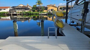 A dock with a small step leading into the water, surrounded by calm water reflecting nearby buildings and vegetation. - Tropical Waterfront Pool Home, Private Dock, Kayaks, Direct Access to Tampa Bay! (Apollo Beach)