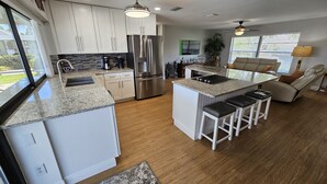 A modern kitchen with white cabinets, a stainless steel refrigerator, a granite countertop, and a bar area with stools. - Tropical Waterfront Pool Home, Private Dock, Kayaks, Direct Access to Tampa Bay! (Apollo Beach)