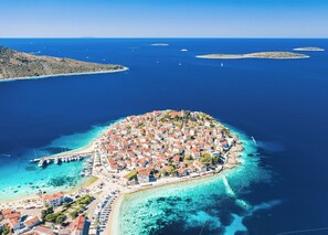 Vista aérea de un pueblo costero con una densa agrupación de edificios, un puerto deportivo y aguas azules cristalinas.