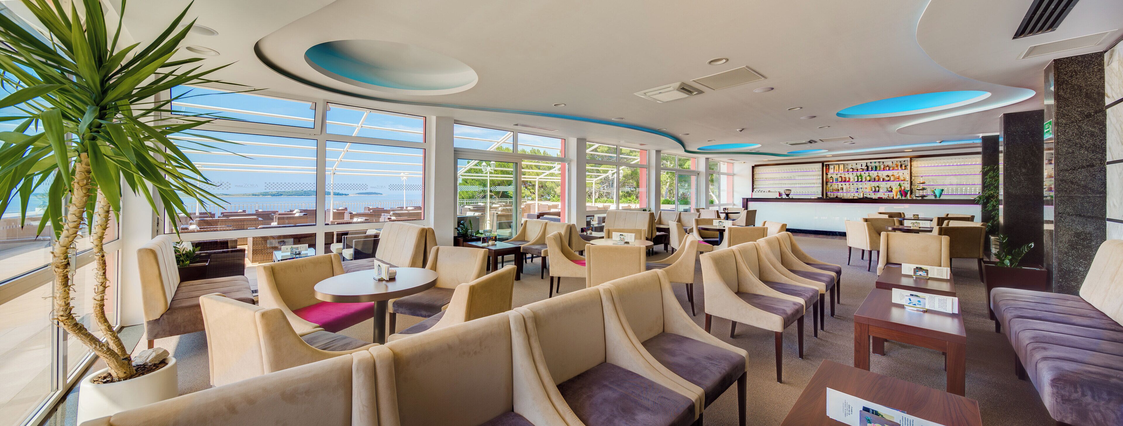 Ein modernes Restaurant mit hohen Decken, großen Fenstern und einer Bar.