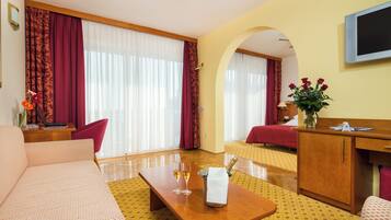 A hotel room with a sofa, a wooden desk, a TV, a bed, and a window with curtains.