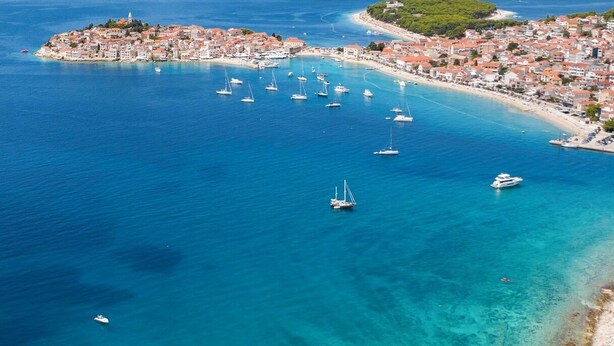 An aerial view of a coastal town with a marina filled with sailboats, a beach, and a small island with buildings. - Hotel Zora (Primosten)