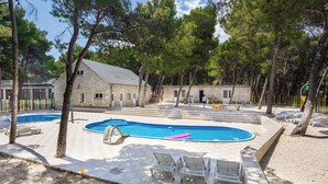 Una piscina con lettini, un edificio in pietra e alberi.