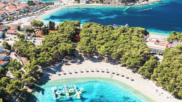 Una località costiera con spiaggia, acque blu cristalline e una piccola isola con edifici.
