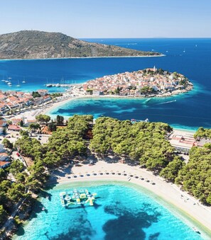 Une ville côtière dotée d’une plage, d’une eau cristalline et d’une petite île abritant des bâtiments.