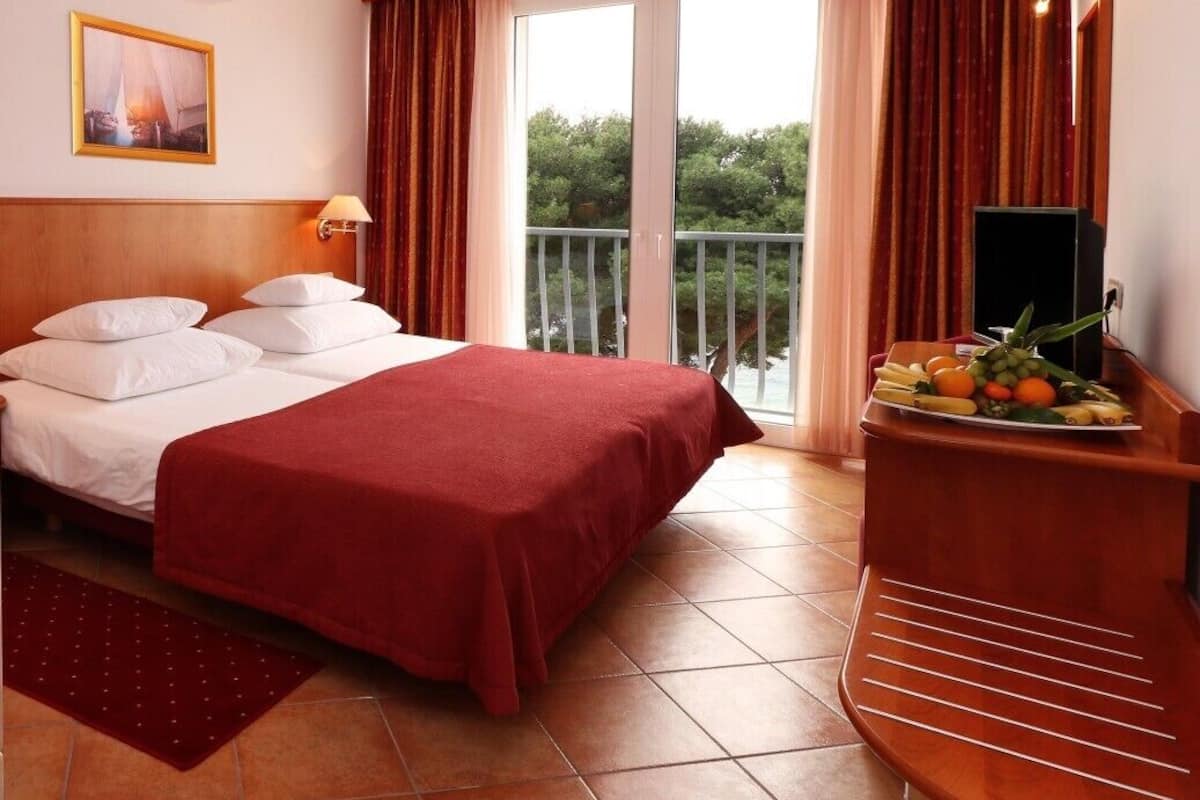 A hotel room with a bed, a TV, a fruit basket, and a balcony with curtains.