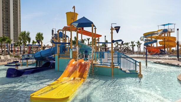 A water park with multiple slides and water features, surrounded by palm trees and a pool area.