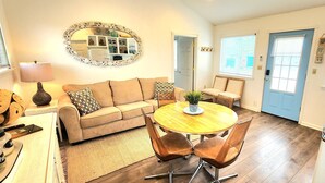 A cozy living room with a sofa, a coffee table, and a dining area with chairs. - Lake View Cottage (Three Mile Bay)