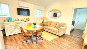 A compact living space with a dining area, sofa, and a television mounted on the wall. - Lake View Cottage (Three Mile Bay)