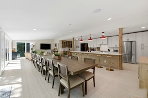 Una cocina moderna con una isla central, taburetes de bar y un comedor con una mesa larga.