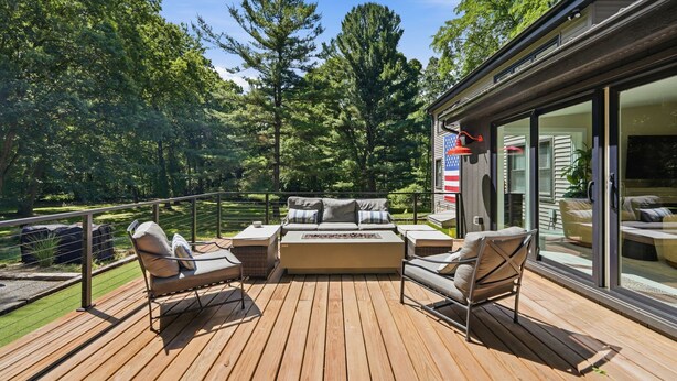A deck with outdoor furniture, a glass-enclosed room, and a view of trees.
