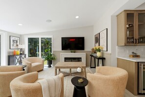 A modern living room with a fireplace, comfortable seating, a flat-screen TV, and a kitchen area with cabinets. - Hideaway - Pickleball Court, Private Pool, Hot Tub, Sleeps 25! (Michigan City)