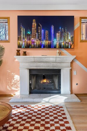 Un salón con chimenea, un tapete a cuadros y un cuadro de un paisaje urbano sobre la repisa.
