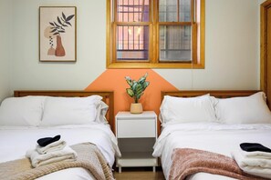 A hotel room with two beds, a nightstand, a potted plant, and a window with a view.