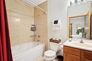 Une salle de bain avec une baignoire, des toilettes et un lavabo. On y trouve des articles de toilette accrochés au mur et un panier rempli de serviettes.