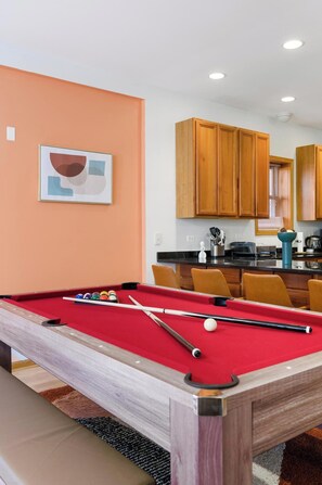 A pool table in a room with wooden cabinets and a kitchen area in the background.