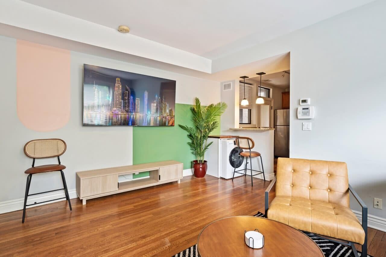 A modern living room with hardwood flooring, a large cityscape painting, a potted plant, a sofa, and a coffee table.