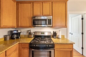 A kitchen with wooden cabinets, a stainless steel microwave, a gas stove, and a coffee maker.