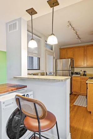 A compact kitchen with wooden cabinets, a built-in washer and dryer, and pendant lighting.
