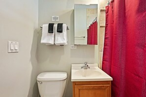 A bathroom with a toilet, sink, and mirror. There are two towels hanging on the wall.