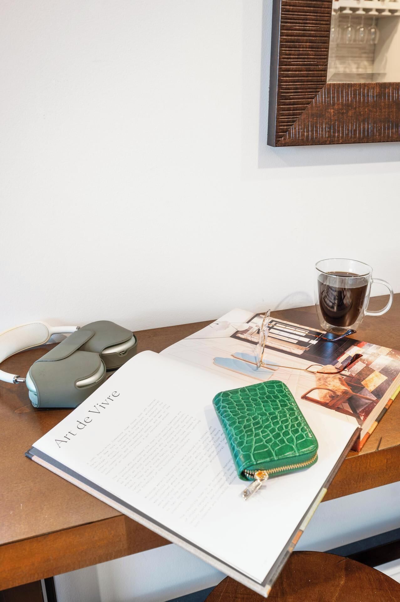 Een bureau met een notitieboek, een groene pennenetui, een paar brillen, een koffiekop en een telefoon.