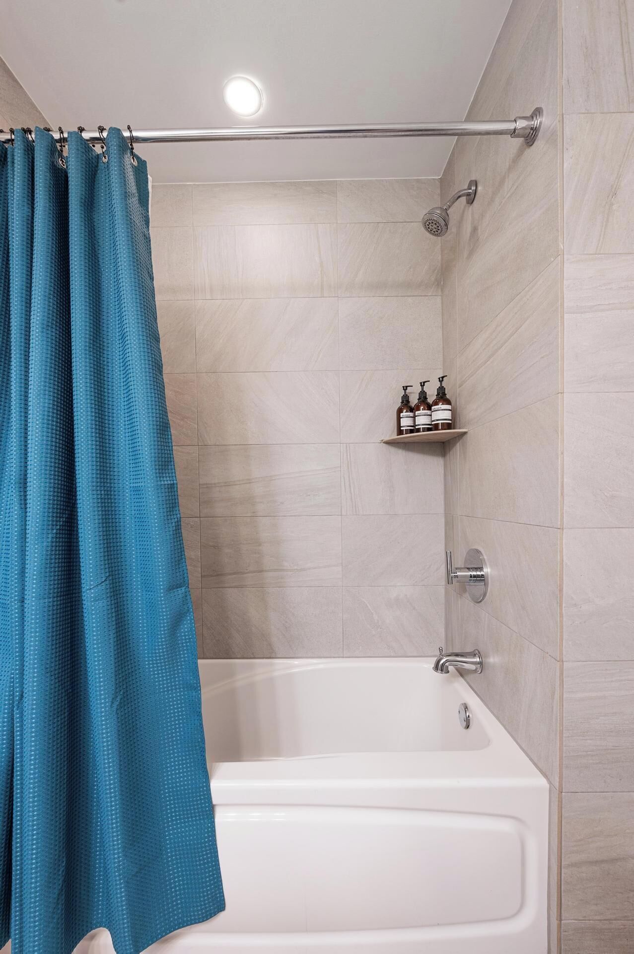 A modern bathroom with a bathtub, shower, and a shelf with toiletries.
