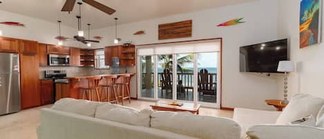 Cozinha moderna com armários de madeira, micro-ondas e uma grande ilha com banquetas. Há uma porta de vidro deslizante que dá para uma varanda com vista para o oceano.