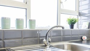 A kitchen with a modern faucet, a window with a view, and three containers labeled sugar, coffee, and tea on the windowsill.