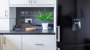 A kitchen with white cabinets, a black refrigerator, a water dispenser, a small potted plant, and a digital device on the counter.