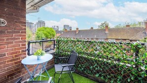 A balcony with a table and chairs, a potted plant, and a view of the cityscape.