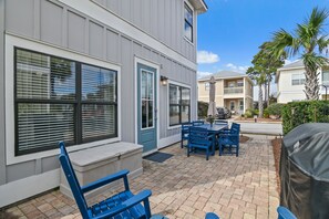 A patio with blue chairs and a table, a covered grill, and a building with large windows and a door. - 🌊 Sundaze 30A – Walk to Beach-4 Bikes Included 🚲 (Santa Rosa Beach)