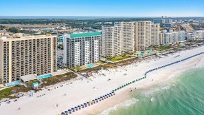 A beachfront hotel with multiple high-rise buildings, a sandy beach, and a long row of umbrellas.