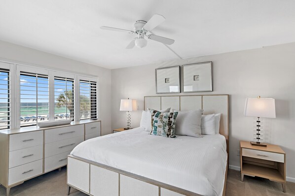A bedroom with a bed, two bedside tables with lamps, a ceiling fan, and a window with blinds.