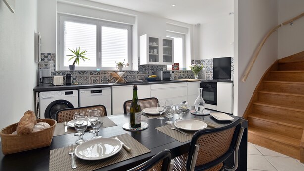 Une cuisine moderne avec un coin repas, comprenant un escalier en bois, un lave-linge et une table à manger pour quatre personnes.