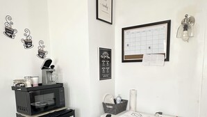Une petite pièce propre, avec un bureau, une chaise et un réfrigérateur noir. Les murs sont décorés et il y a un calendrier accroché.