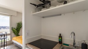 A compact kitchen with a built-in stove, a sink, and a window overlooking a cityscape. - Le Studio de l'Ange - Vue imprenable (Rennes)