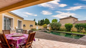 A patio with a pool, wooden deck, and a table with chairs.