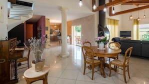 A spacious living area with a wooden dining table, chairs, a fireplace, and a modern kitchen in the background.