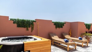 Een dakterras met een jacuzzi, lounge fauteuils en een houten kast.