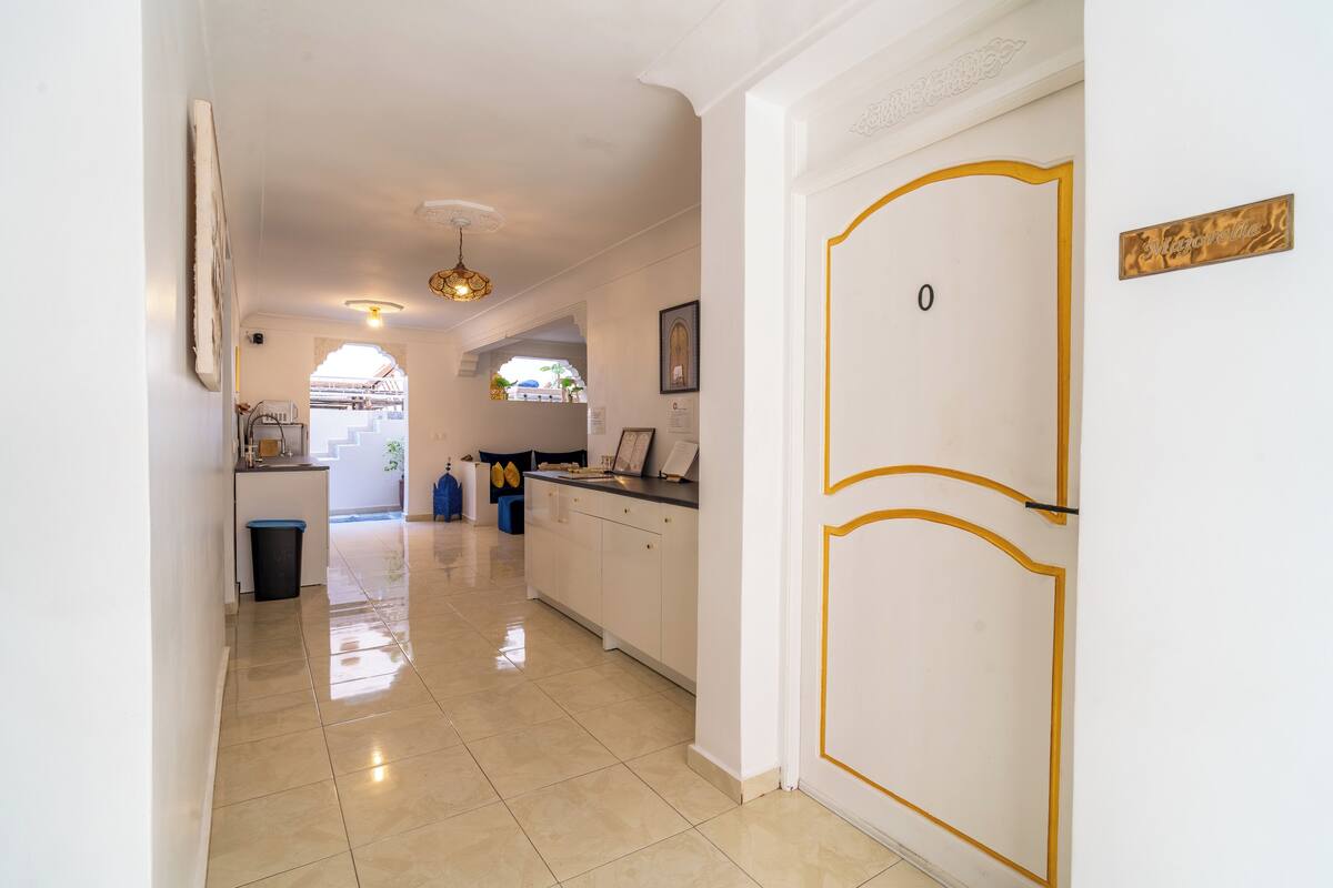 A hallway with a white door, a kitchen area, and a view into another room.