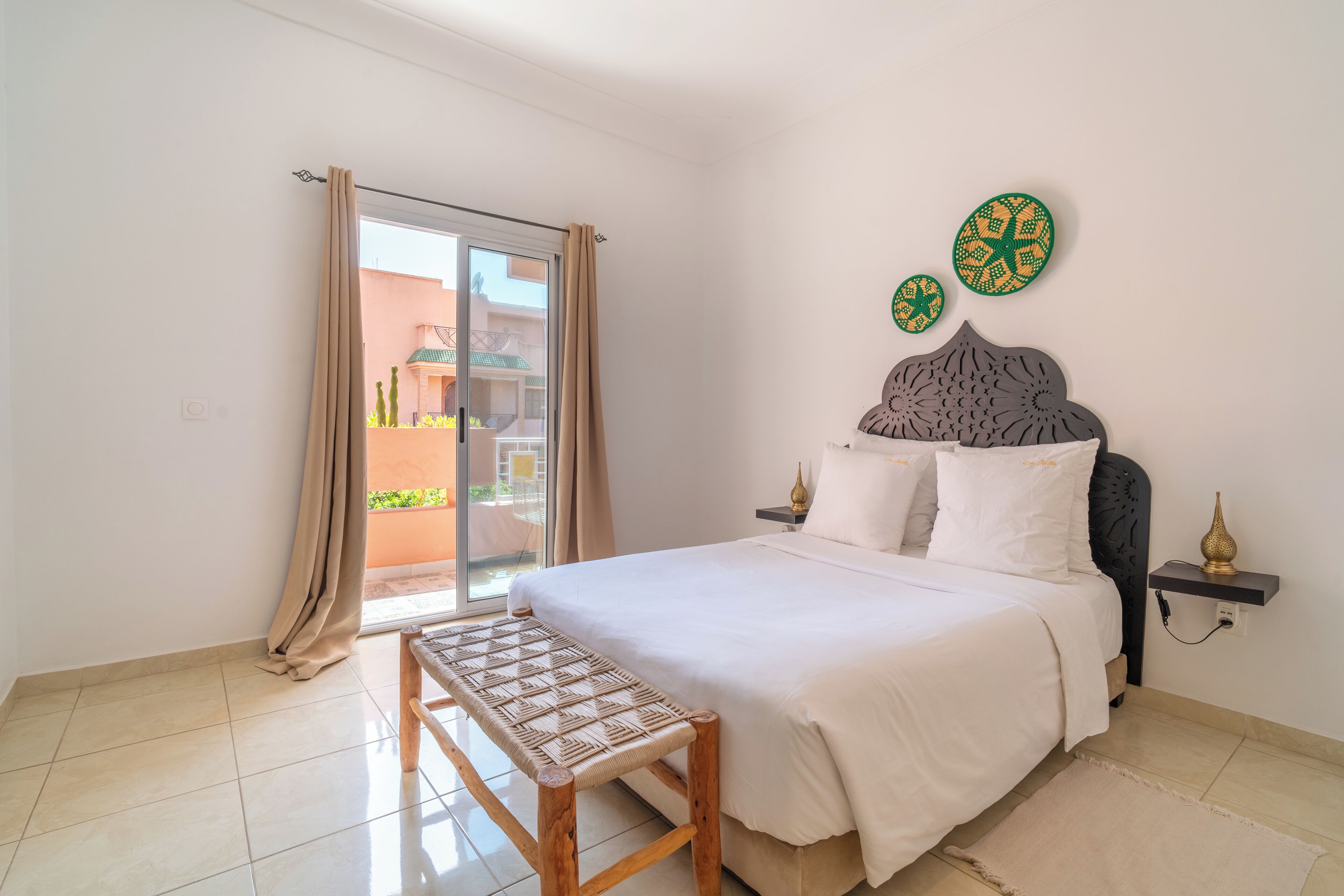 A bedroom with a bed, bench, curtains, and decorative wall art.