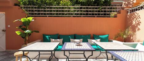 An outdoor seating area with a table and chairs, a sofa with cushions, and a potted plant.
