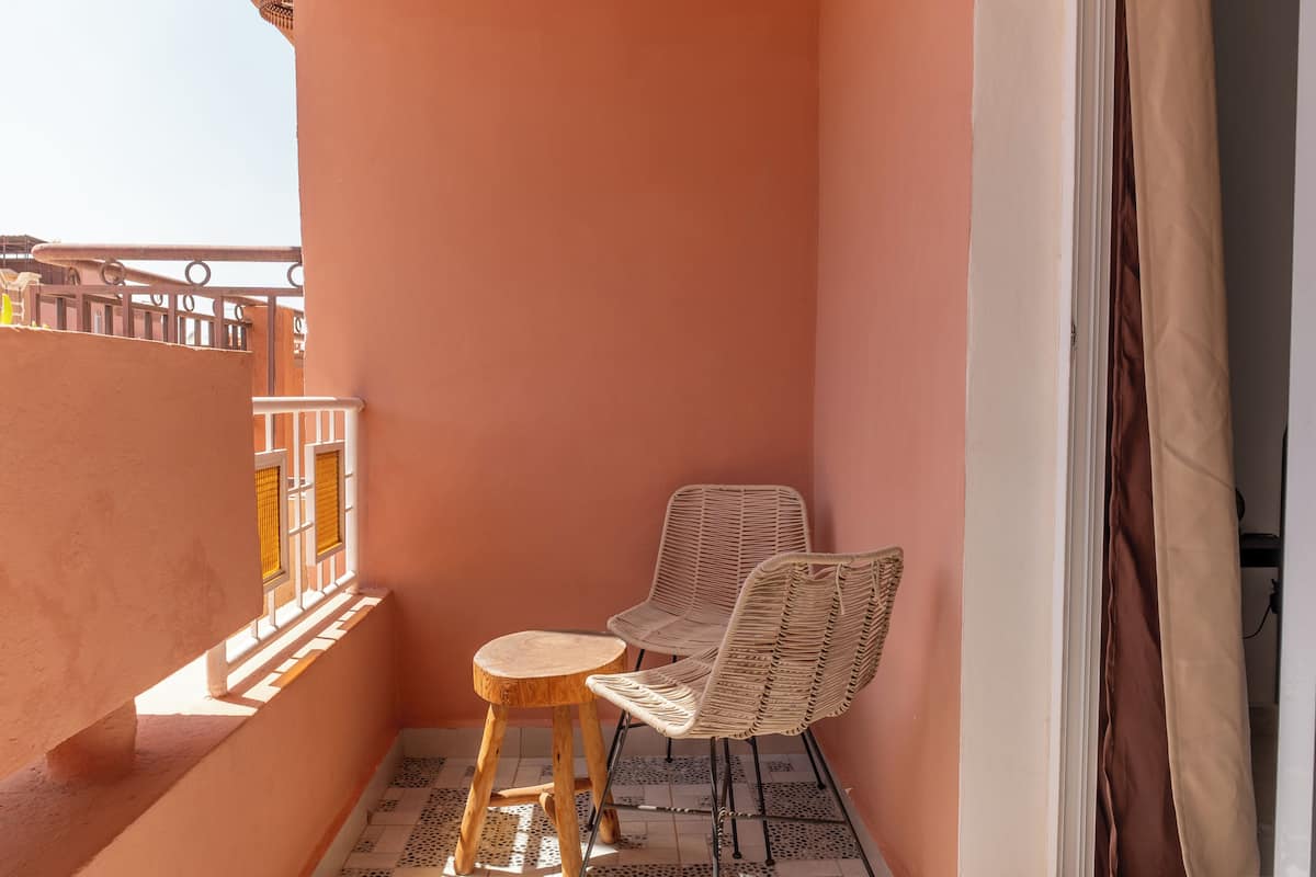 A balcony with a table and two chairs, a tiled floor, and a pink wall.