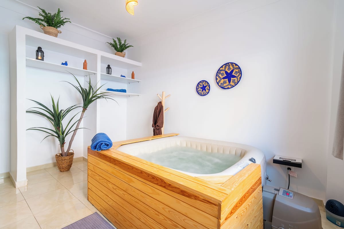 A wooden bathtub in a room with shelves, a plant, and decorative plates.